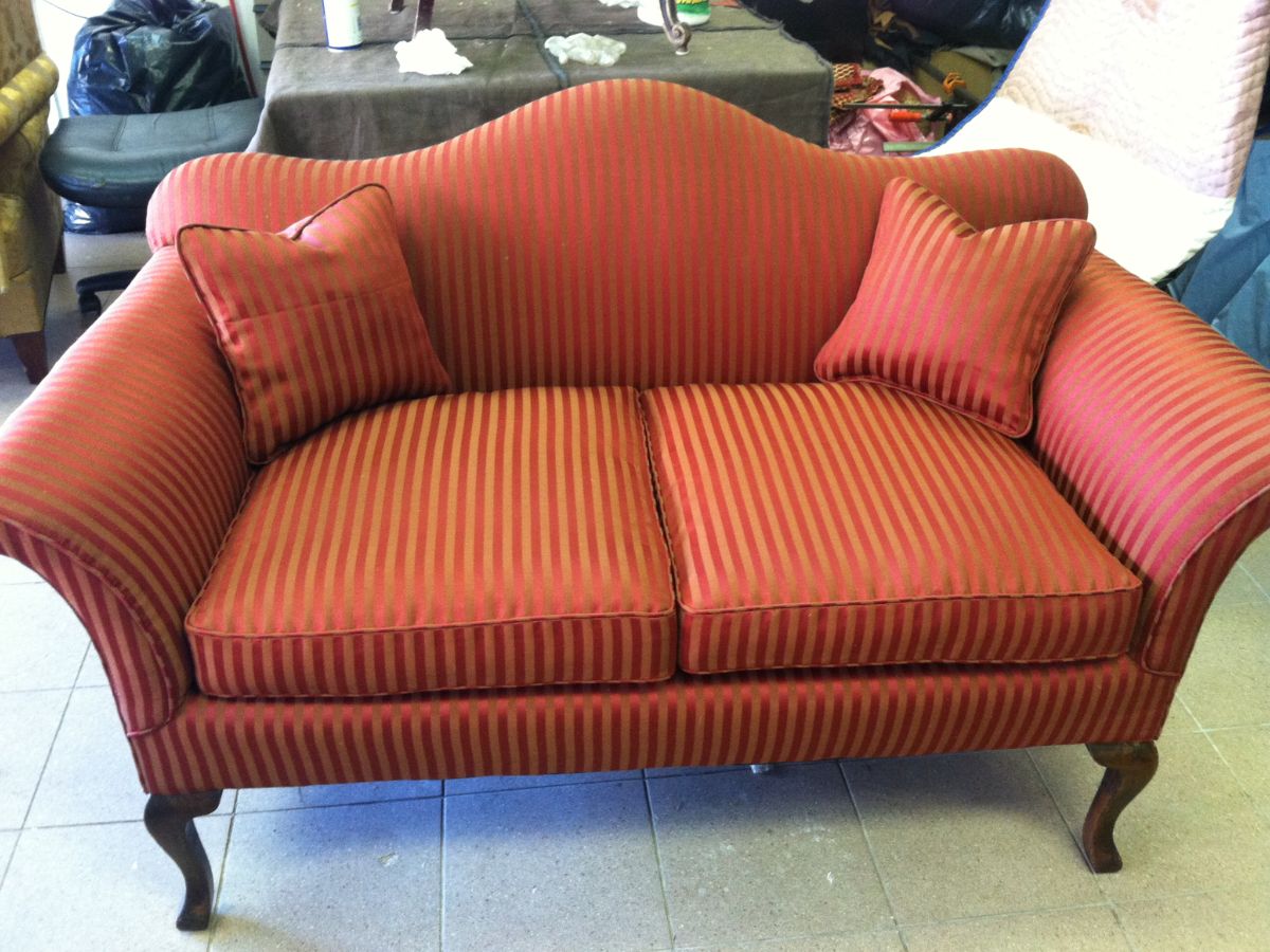 Elegant vintage red sofa with striped fabric, two matching cushions, and curved wooden legs, placed on a tile floor.