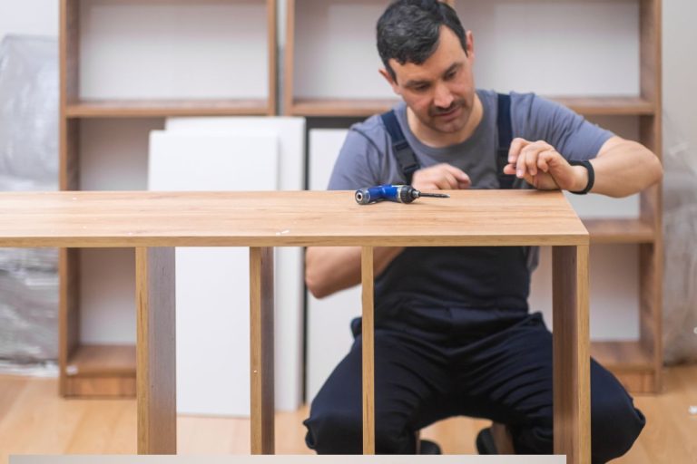 A person is assembling furniture, focused on a wooden tabletop with a screwdriver in front, surrounded by shelves and materials.